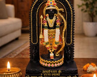 May include: A black statue of a deity holding a golden bow and arrow, adorned with colorful jewels and white beads. The base features gold Hindi text that reads Ayodhya ke Ram Lalla and Hare Rama Hare Rama Rama Rama Hare Hare.