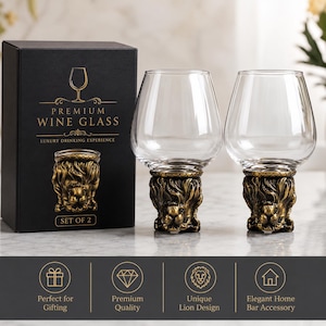 May include: Two clear glass wine glasses with gold-toned metallic bases shaped like lion heads. The glasses are displayed next to a black rectangular box featuring the text PREMIUM WINE GLASS and an illustration of the lion-themed glass base.