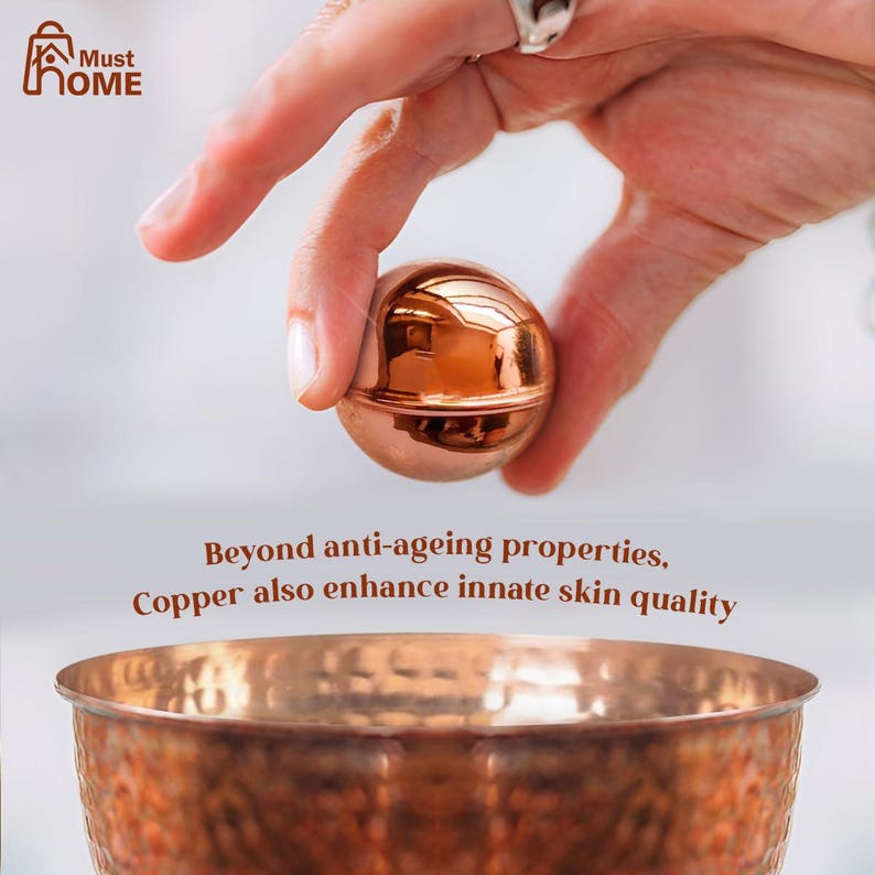 May include: A polished copper sphere held above a hammered copper bowl. The text reads: Must HOME. Beyond anti-ageing properties, Copper also enhance innate skin quality. The metallic surface reflects light, showing a warm, reddish-brown tone.