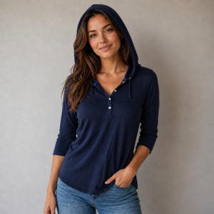 Può includere: Una maglia a maniche lunghe con cappuccio in blu navy scuro, caratterizzata da un'abbottonatura parziale con quattro piccoli bottoni bianchi. Il capo è realizzato in un tessuto leggero e morbido e include un cappuccio con cordini in tinta.