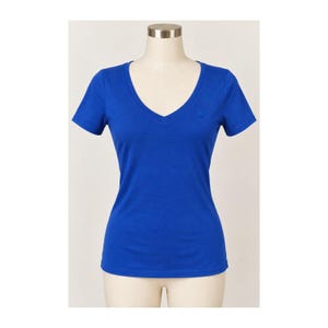 May include: A solid royal blue short-sleeve t-shirt featuring a deep V-neckline. The garment is displayed on a mannequin torso and includes a small, tonal embroidered logo detail on the upper left chest area of the fabric.