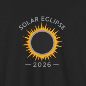 Pode incluir: T-shirt preta com um design de eclipse solar. O gráfico apresenta um sol amarelo com um centro escuro, as palavras "SOLAR ECLIPSE" acima e o ano "2026" abaixo. A t-shirt é feita de um material macio.