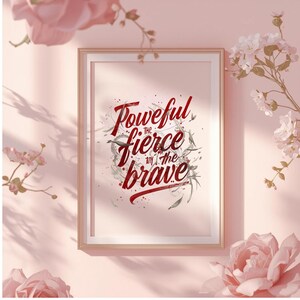 May include: Framed art print with the words "Powerful, the fierce, and the brave" in a stylized red script. The print is in a gold frame, set against a pink background with floral accents.