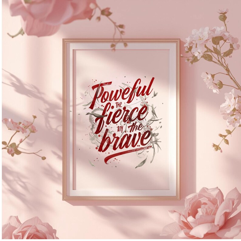 May include: Framed art print with the words "Powerful, the fierce, and the brave" in a stylized red script. The print is in a gold frame, set against a pink background with floral accents.