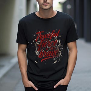 May include: Black t-shirt with the red text "Powerful, the Fierce, in the Brave" in a stylized font. The design includes white and tan decorative elements. The shirt is a crew neck style.