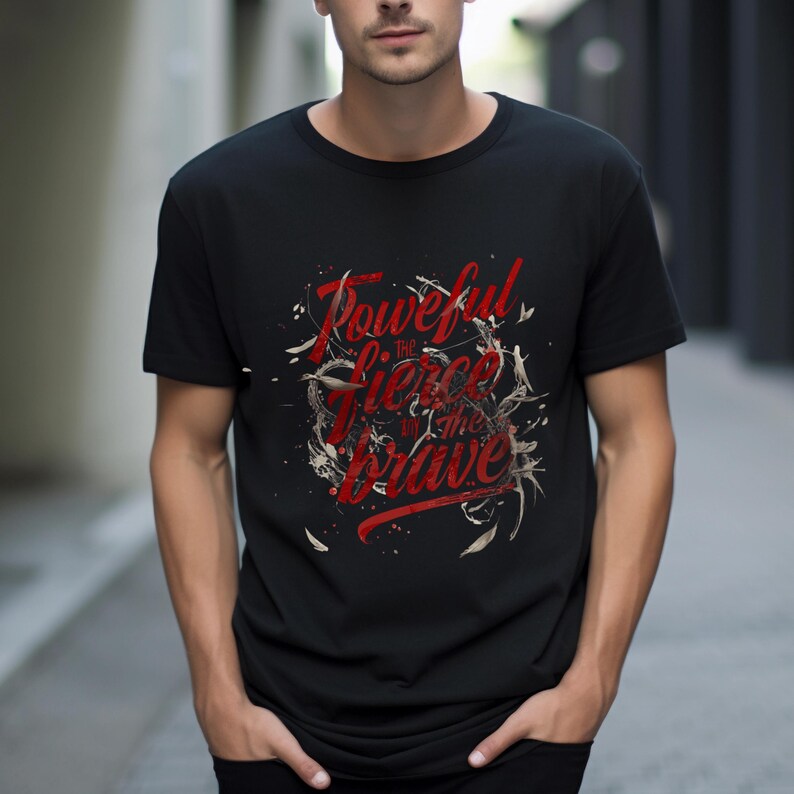 May include: Black t-shirt with the red text "Powerful, the Fierce, in the Brave" in a stylized font. The design includes white and tan decorative elements. The shirt is a crew neck style.