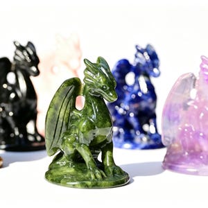 May include: A collection of small dragon figurines carved from various polished stones, including green, black, blue, purple, and orange varieties. Each dragon features detailed wings, a pointed snout, and a seated posture on a smooth base.
