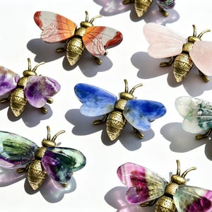 May include: A collection of bee-shaped ornaments featuring antique brass-toned metal bodies and wings crafted from various polished gemstones, including amethyst, rose quartz, sodalite, moss agate, and multi-colored fluorite in various hues.