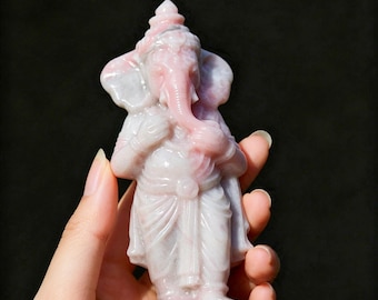 May include: A carved light pink and white stone figurine of the deity Ganesha standing on a circular base. The sculpture features the elephant-headed figure with a trunk curved to the left, wearing traditional attire and a crown, with smooth textures.
