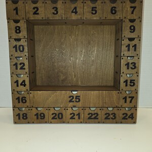 May include: A wooden advent calendar with a rectangular frame and 25 numbered compartments. The numbers 1-25 are printed in black. The calendar is made of light brown wood.