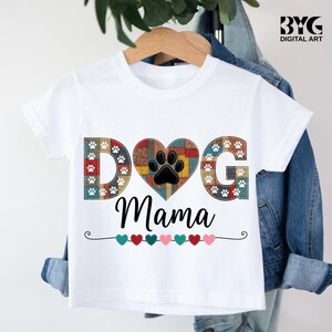 May include: White t-shirt with the words "DOG Mama" in a playful font. The word "DOG" is in a patchwork design with paw prints, and the heart-shaped "O" features a black paw print. A row of colorful hearts decorates the bottom.
