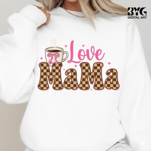 May include: White sweatshirt with a graphic design that says "Love Mama." The word "Love" is in pink script, and "Mama" is in a brown and tan checkerboard pattern. A coffee cup with a pink bow is on the left.