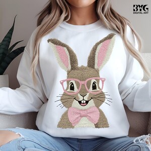 May include: White sweatshirt featuring an embroidered bunny wearing pink glasses and a pink bow tie. The bunny has brown fur and long ears with pink inner ears. The design is a cute and whimsical Easter theme.