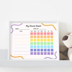 May include: A framed "My Chore Chart" with a rainbow-colored grid for tracking tasks. The chart includes spaces for the name and week of the tasks. A stuffed dog toy sits on a shelf next to the chart.