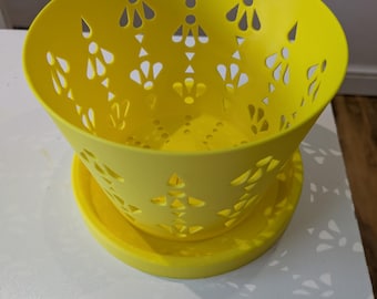 May include: A vibrant yellow bowl and matching saucer. The bowl features decorative cut-out patterns around its curved sides. The bowl sits on a circular saucer. The set is made of a solid material, possibly plastic or ceramic.