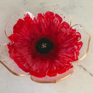 May include: A flower-shaped dish made of translucent resin with vibrant red petals that transition to a solid black center. The edges of the petals are outlined in gold, and small gold flakes are embedded throughout the clear resin sections.