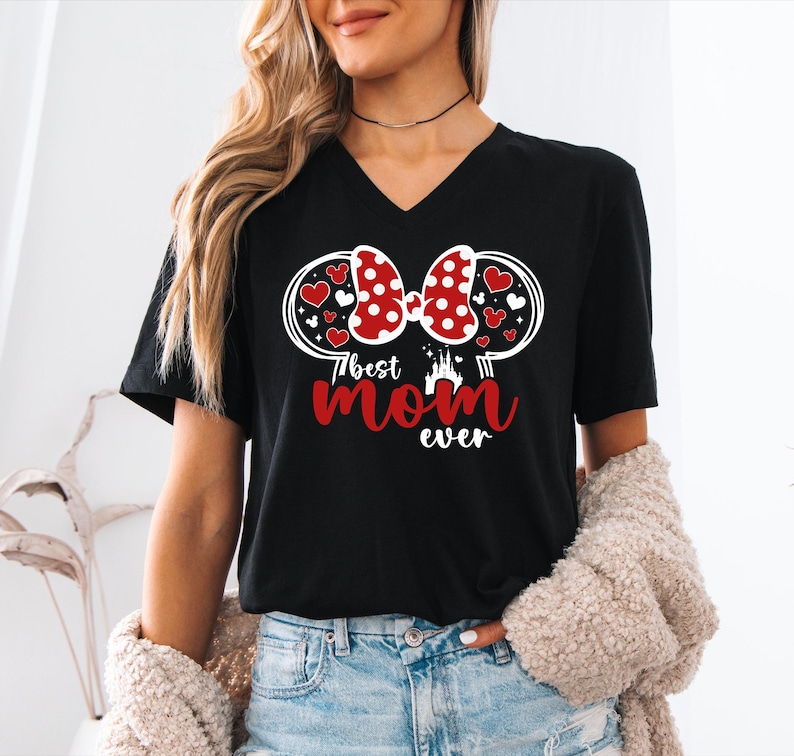 May include: Black V-neck t-shirt with a graphic design featuring a red polka-dot bow, hearts, and the text "Best Mom Ever" in red. The design includes a castle silhouette. The shirt is a casual wear item.
