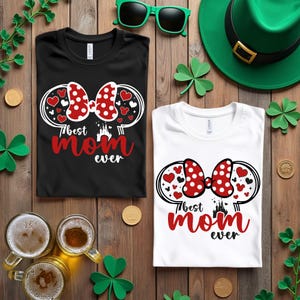 May include: Two t-shirts, one black and one white, with a graphic that says "Best Mom Ever." The graphic includes a red polka dot bow, hearts, and a castle silhouette. Green sunglasses and a green hat are also visible.