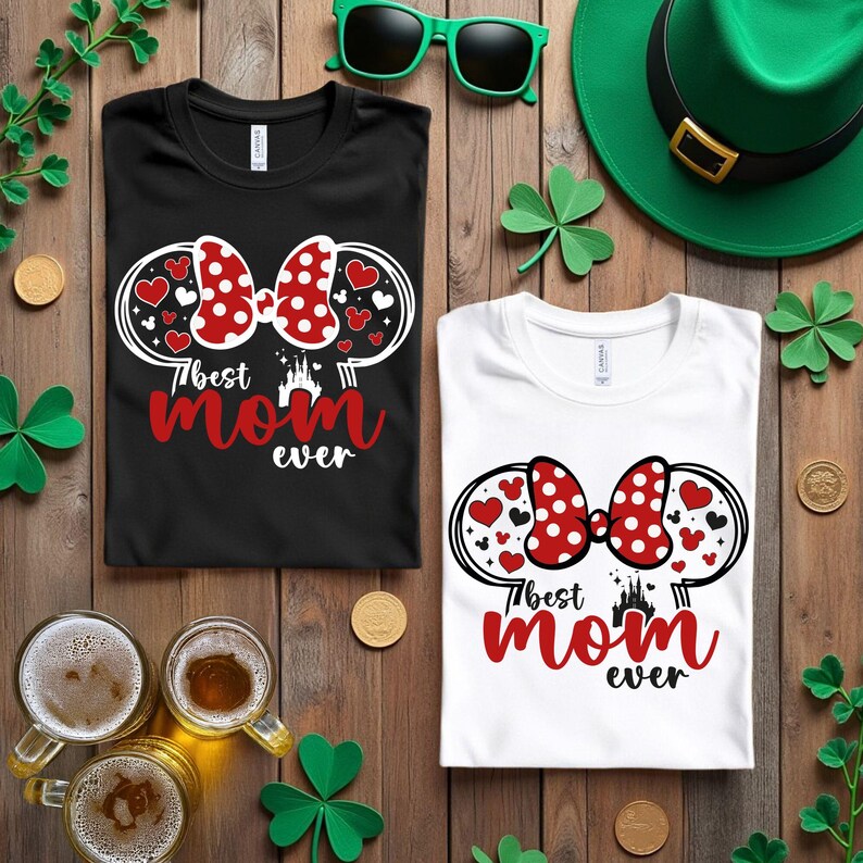 May include: Two t-shirts, one black and one white, with a graphic that says "Best Mom Ever." The graphic includes a red polka dot bow, hearts, and a castle silhouette. Green sunglasses and a green hat are also visible.