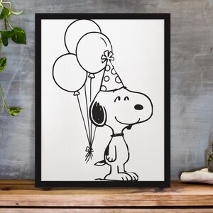 May include: Black and white framed print featuring a cartoon dog wearing a party hat and holding balloons. The dog is smiling and the balloons are tied together with a bow. The artwork is displayed on a wooden surface.