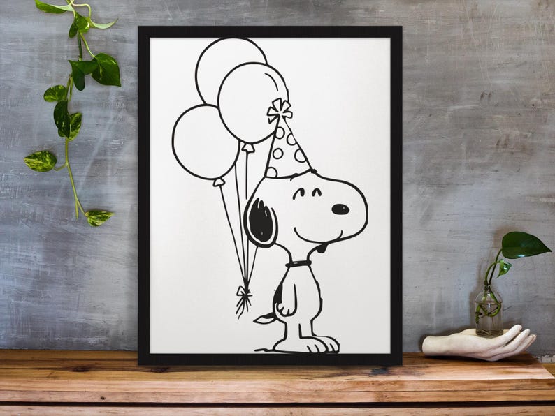 May include: Black and white framed print featuring a cartoon dog wearing a party hat and holding balloons. The dog is smiling and the balloons are tied together with a bow. The artwork is displayed on a wooden surface.