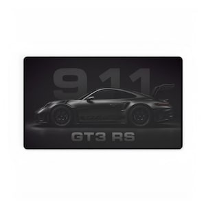 May include: A rectangular black desk mat featuring a side profile of a dark gray sports car. The text 911 is printed in large, bold, dark gray font in the background, and the text GT3 RS is printed in a smaller, bold, dark gray font below the car.