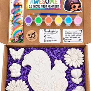May include: A craft kit in a cardboard box containing a squirrel-shaped plaster figure, two flower shapes, a butterfly, a heart, and a small creature. Includes six paint pots, a brush, a sticker of a hedgehog, and a card reading SOMETIMES YOU FORGET YOU ARE AWESOME SO THIS IS YOUR REMINDER.