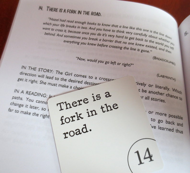 May include: A white card with black text that reads "There is a fork in the road." The card is numbered 14 in the bottom right corner. The card is partially covering a book page with text about a story and a reading.