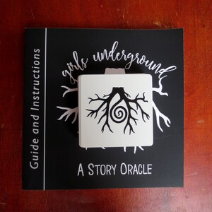 May include: A black and white card with a tree root design and the text "girls underground A STORY ORACLE" on a black background. The card is part of a story oracle deck.