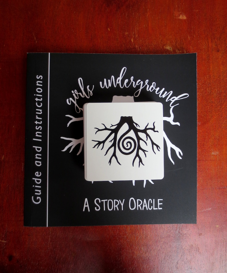 May include: A black and white card with a tree root design and the text "girls underground A STORY ORACLE" on a black background. The card is part of a story oracle deck.
