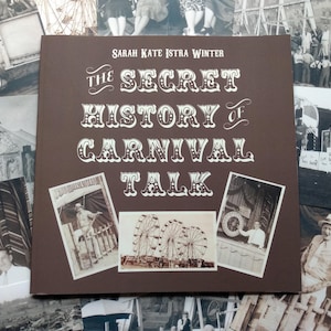May include: A brown book with the title "The Secret History of Carnival Talk" by Sarah Kate Istra Winter. The book cover features images of a carnival, including a Ferris wheel, a carousel, and a booth.