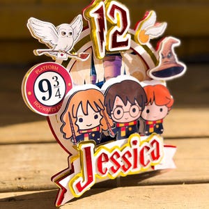 Könnte beinhalten: Ein farbenfroher Tortenaufsatz mit Harry-Potter-Figuren, einer weißen Eule und der Zahl 12. Der Aufsatz enthält den Text "Jessica" und "Platform 9 3/4". Das Design ist mit roten, gelben und weißen Akzenten versehen.