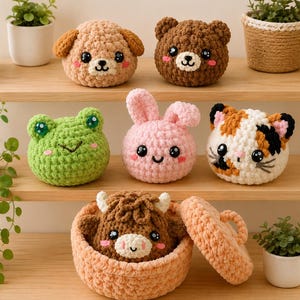 May include: A collection of six round, crocheted plush animal figures including a tan dog, brown bear, green frog, pink rabbit, calico cat, and a brown highland cow inside a matching lidded basket, all featuring black plastic eyes and pink cheeks.