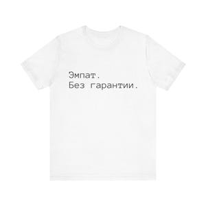 Könnte beinhalten: Weißes T-Shirt mit schwarzem Text. Der Text, in einer einfachen serifenlosen Schrift, lautet "Эмпат. Без гарантии." Das Shirt hat kurze Ärmel und einen Rundhalsausschnitt. Der Stoff scheint eine weiche Baumwollmischung zu sein.