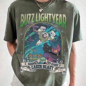 Puede incluir: Camiseta verde musgo con un gr&aacute;fico de Buzz Lightyear de Toy Story de Disney. El dise&ntilde;o incluye las palabras "Buzz Lightyear", "Disney", "Toy Story" y "Laser Blast". El gr&aacute;fico es en tonos de verde, azul, morado y blanco.