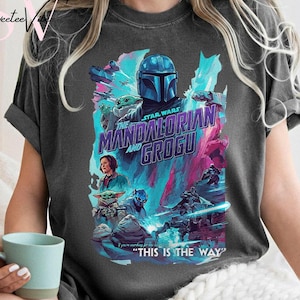 May include: Dark gray t-shirt featuring a colorful graphic from the Star Wars series, "The Mandalorian and Grogu." The design includes characters, the show's title, and the phrase "This is the Way."