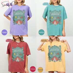 May include: Four oversized t-shirts in violet, seafoam, crimson, and mustard. Each shirt features a graphic of Ariel from "The Little Mermaid" with the text "The Little Mermaid".