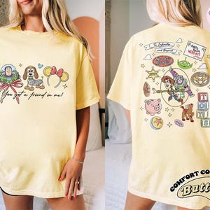 May include: Yellow t-shirt with front and back graphics. The front features Buzz Lightyear, a dog, and Minnie Mouse ears with text "You got a friend in me!". The back has Woody, Buzz, and other Toy Story characters.