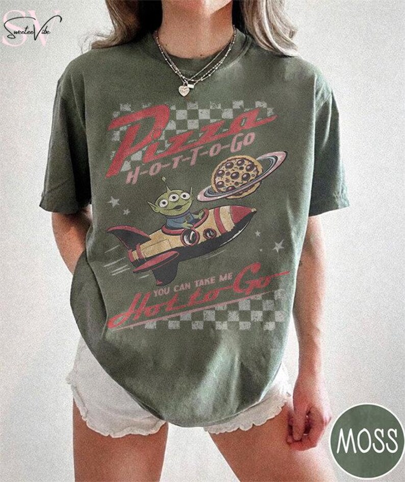 May include: Moss green t-shirt with a graphic featuring a cartoon alien in a rocket ship, a pizza planet, and the text "Pizza H-O-T-T-O-Go". The shirt has a vintage, distressed look.