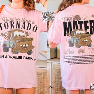 Puede incluir: Camiseta rosa claro con una imagen de dibujos animados de Mate del coche de la pel&iacute;cula Cars. La parte delantera de la camiseta dice "Happier than a Tornado in a Trailer Park". La parte trasera dice "Tow Mater".