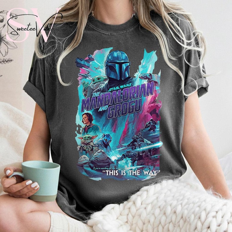 May include: Dark gray t-shirt featuring a colorful graphic from the Star Wars series, "The Mandalorian and Grogu." The design includes characters, the show's title, and the phrase "This is the Way."
