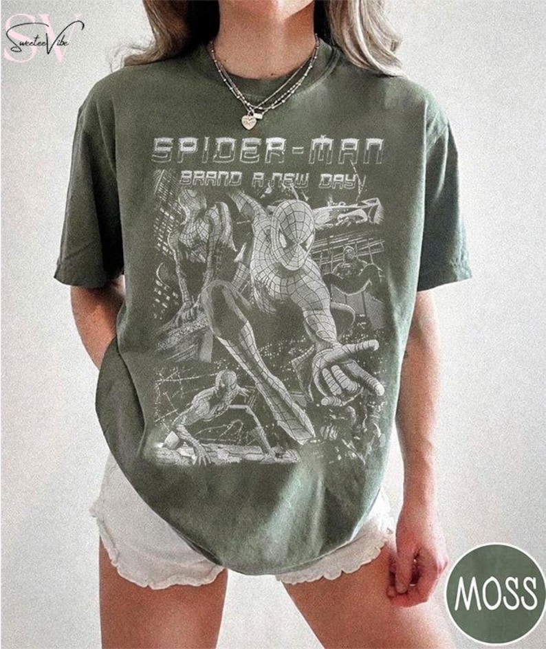 May include: An olive green short-sleeve t-shirt featuring a white graphic print of Spider-Man in various action poses. The text "SPIDER-MAN" and "BRAND A NEW DAY" is printed in a bold, distressed font above the character illustrations.