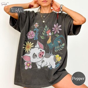 Puede incluir: Camiseta gris oscuro con un dise&ntilde;o de cerdo y gallo de dibujos animados, rodeados de flores. El texto "Next Day Shipping" est&aacute; en la parte superior izquierda. El color "Pepper" se indica en la parte inferior derecha.