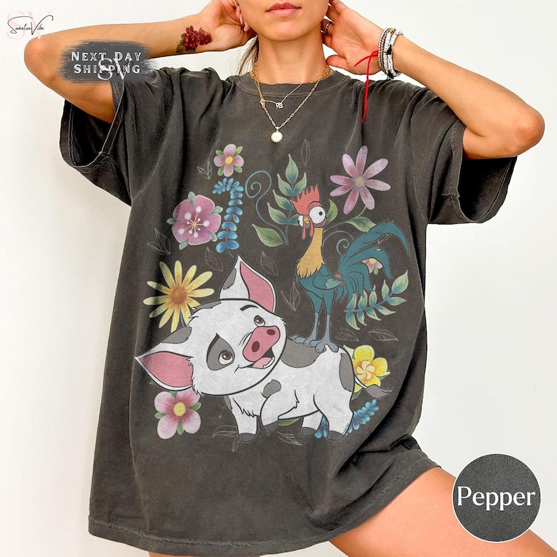 Puede incluir: Camiseta gris oscuro con un dise&ntilde;o de cerdo y gallo de dibujos animados, rodeados de flores. El texto "Next Day Shipping" est&aacute; en la parte superior izquierda. El color "Pepper" se indica en la parte inferior derecha.