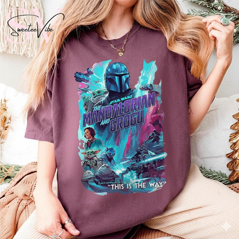 May include: A maroon t-shirt featuring a colorful graphic from the Star Wars series, "The Mandalorian and Grogu." The design includes characters and the phrase "This is the Way."