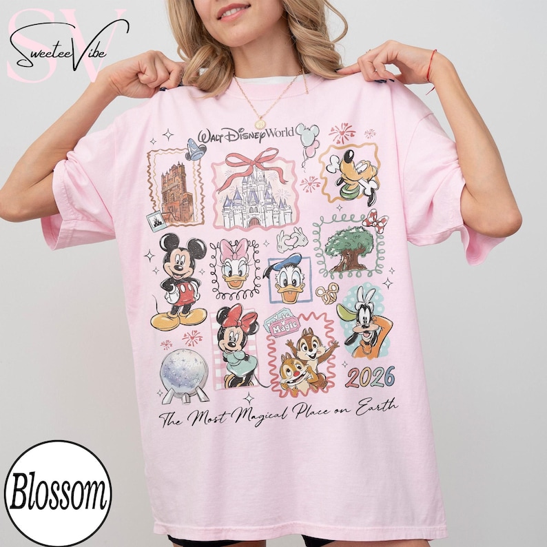 Puede incluir: Camiseta rosa claro con personajes de Disney, incluyendo Mickey y Minnie Mouse. La camiseta muestra "Walt Disney World", "The Most Magical Place on Earth" y el a&ntilde;o "2026". El dise&ntilde;o incluye ilustraciones y elementos decorativos.