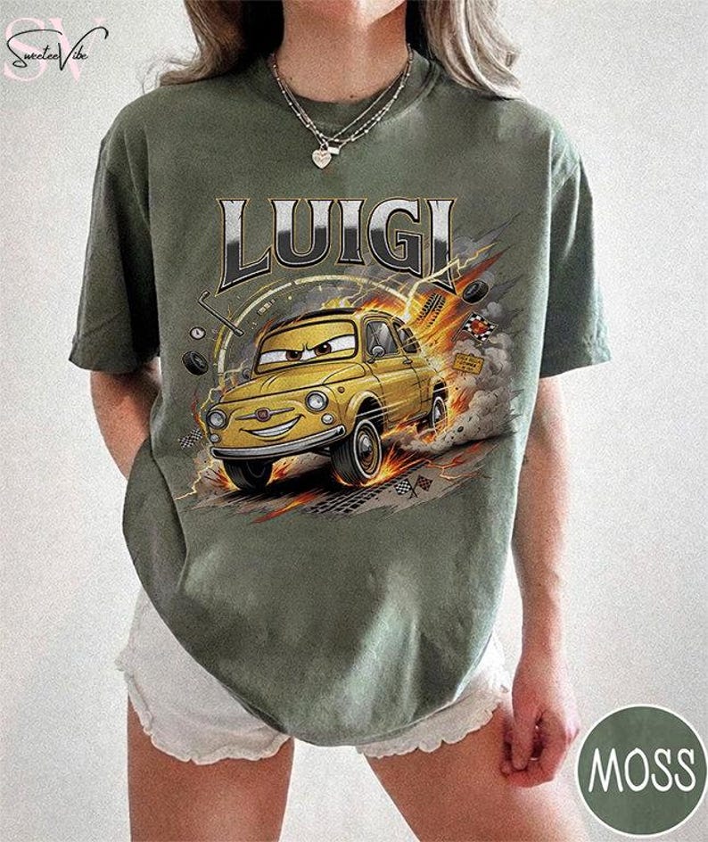May include: Olive green t-shirt featuring the name "LUIGI" above a cartoon image of a yellow car with a smiling face. The car is depicted in motion with flames and tire tracks. The shirt has a crew neck and short sleeves.