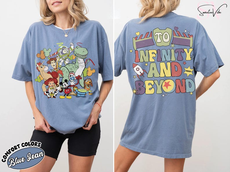 Op de afbeelding: Blauw spijkerbroekkleurig T-shirt met een afbeelding van Toy Story-personages op de voorkant. De achterkant toont de zin "To Infinity and Beyond" in kleurrijke letters, met raket- en steraccenten. Het shirt is een comfort colors-stijl.