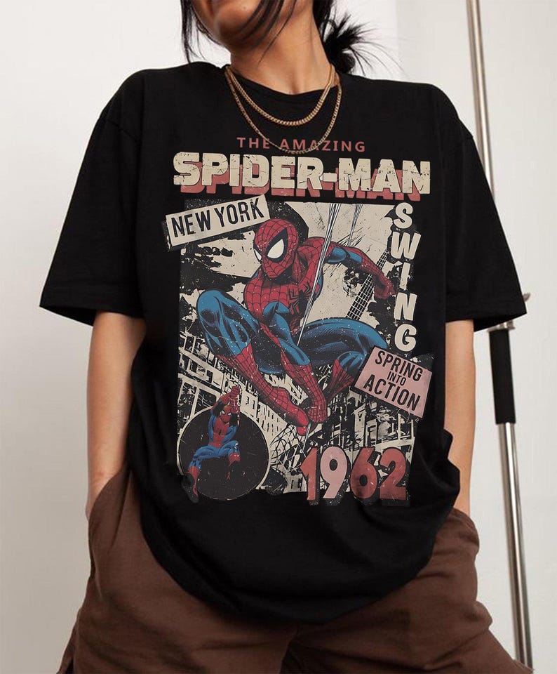 May include: Black t-shirt featuring a vintage Spider-Man graphic. The design includes the text "The Amazing Spider-Man," "New York," and "1962." The graphic shows Spider-Man in action, with red and blue colors.
