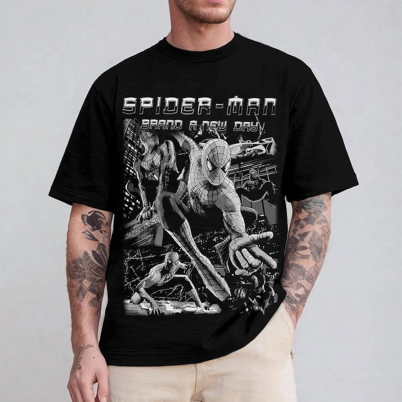 May include: A black short-sleeve t-shirt featuring a graphic print of the comic book character Spider-Man in various action poses. The text "SPIDER-MAN" and "BRAND A NEW DAY" is printed in white above the black and white comic-style illustrations.